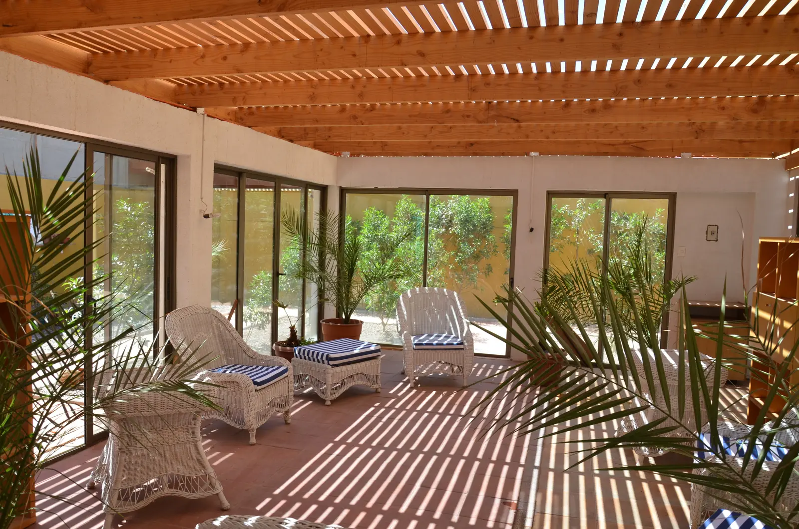 Terraza cerrada con termopanel, techo de madera y mobiliario de mimbre